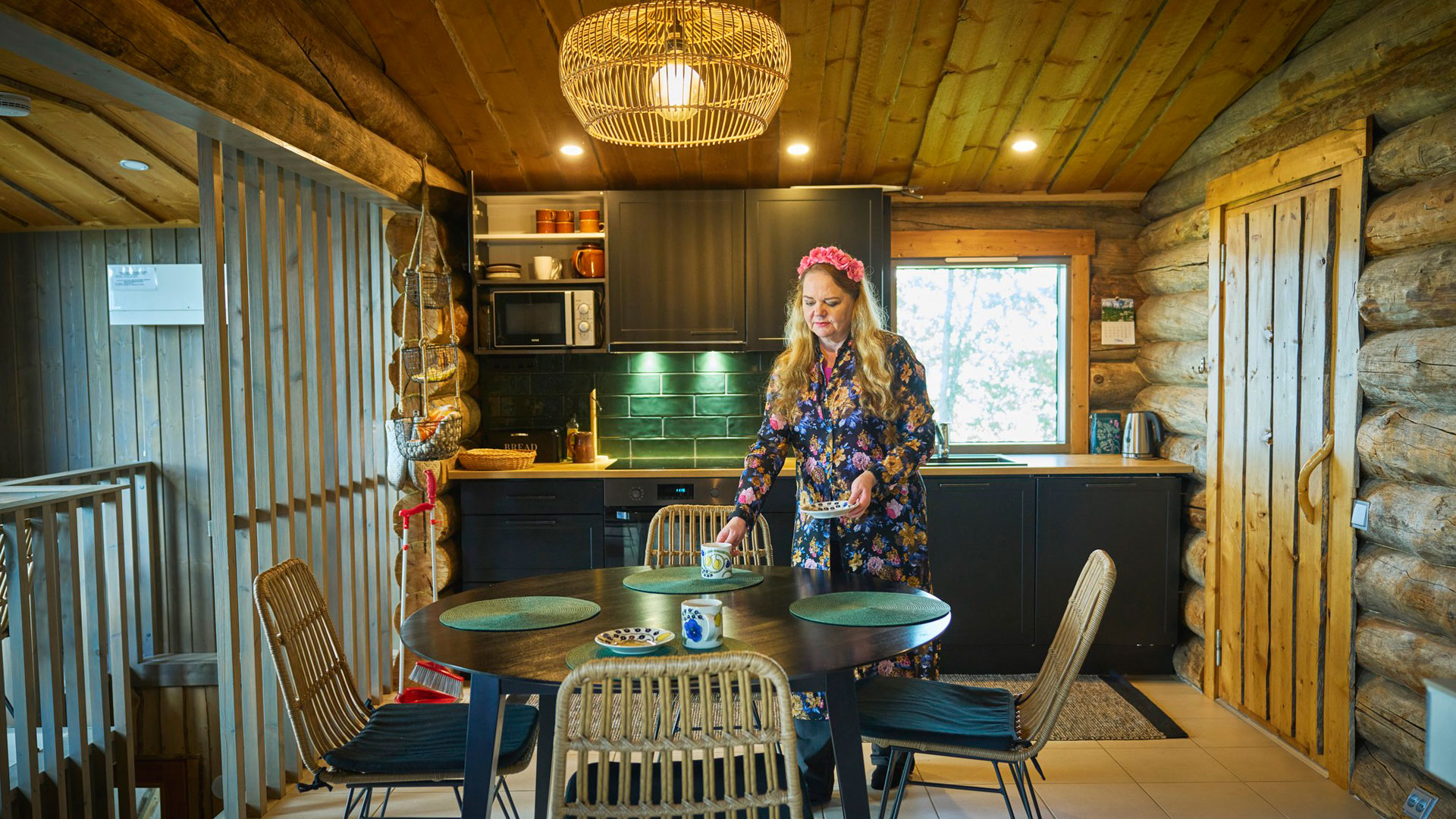 Nainen kattaa pöytää kelomökin keittiössä.