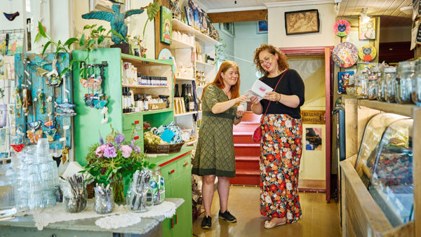 Kaksi hymyilevää naista tutkii kirjaa kaupassa.